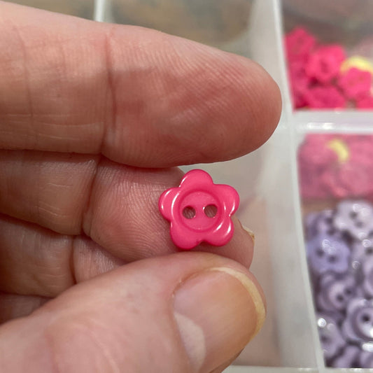 Hand holding a pink flower-shaped object with a container of assorted small items in the background.