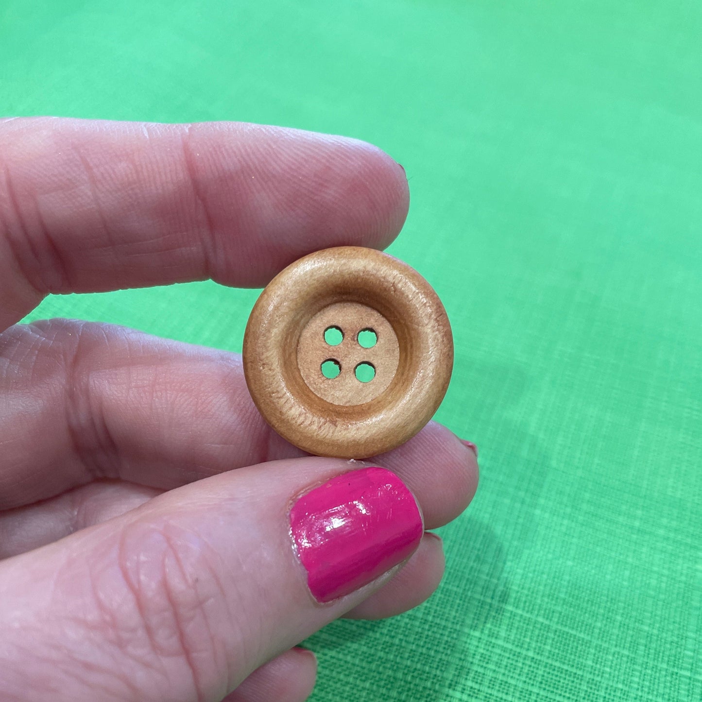Hand holding a wooden button against a green background