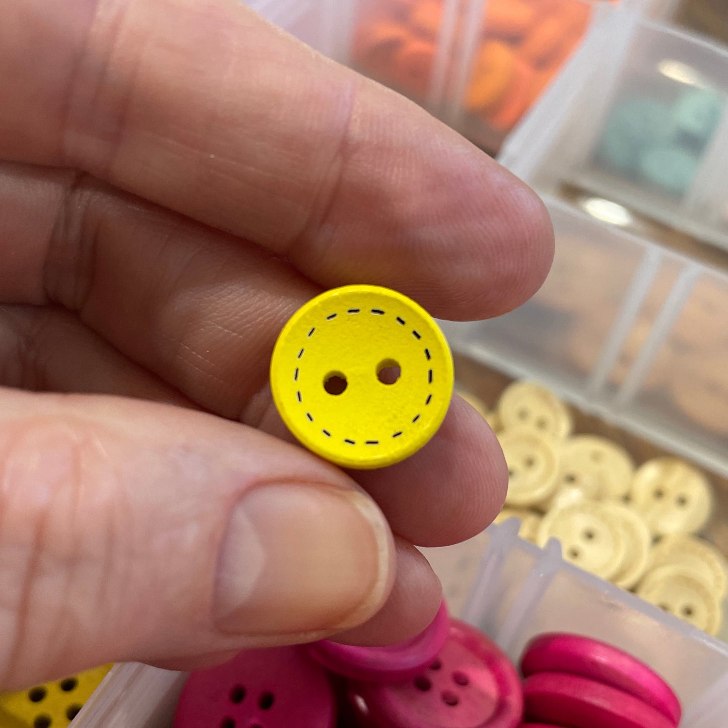 Yellow button held by a hand with a container of pink buttons in the background
