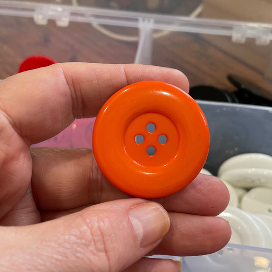 Hand holding an orange button with a blurred background of buttons and packaging.