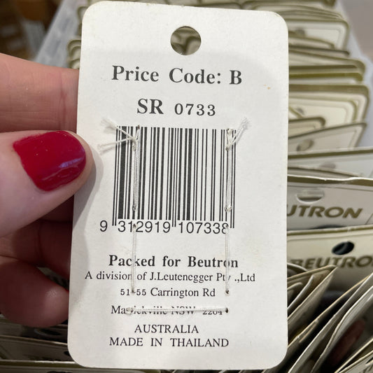 Close-up of a product tag with a barcode and text, held by a hand with red nail polish.