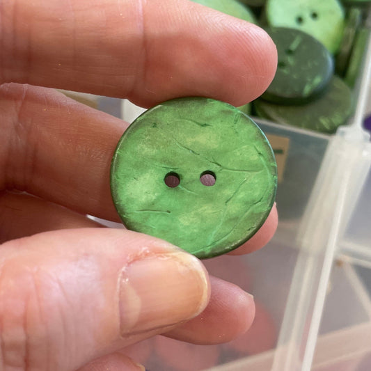 Green button held by a hand with a container of assorted buttons in the background