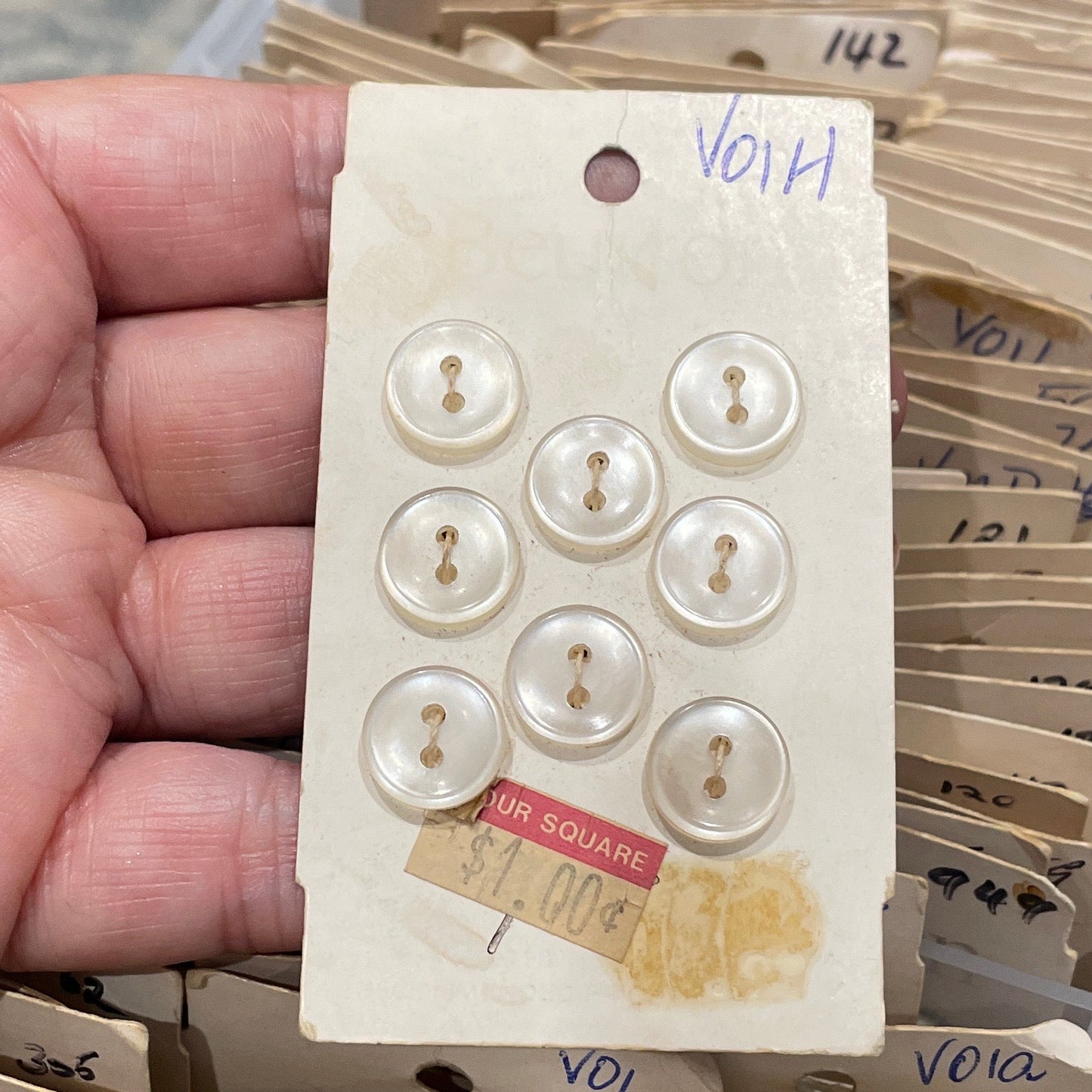 Hand holding a card with pearl buttons against a background of similar cards.