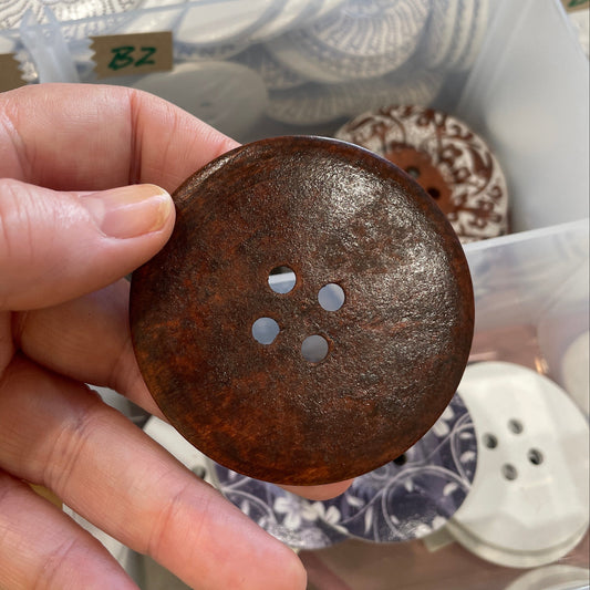Hand holding a rusted metal button with a blurred background of various buttons.