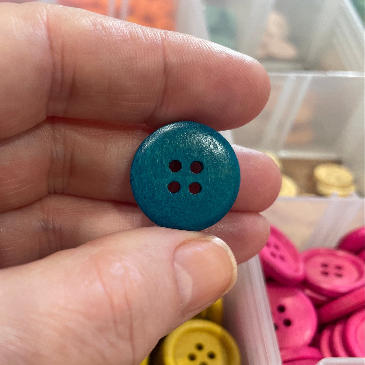 Hand holding a blue button with a container of colorful buttons in the background