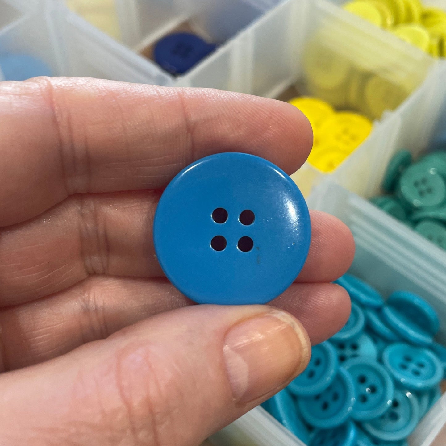 Hand holding a blue button with a container of buttons in the background