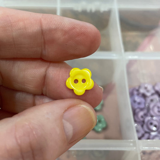 Hand holding a yellow flower-shaped object with a container of similar objects in the background.