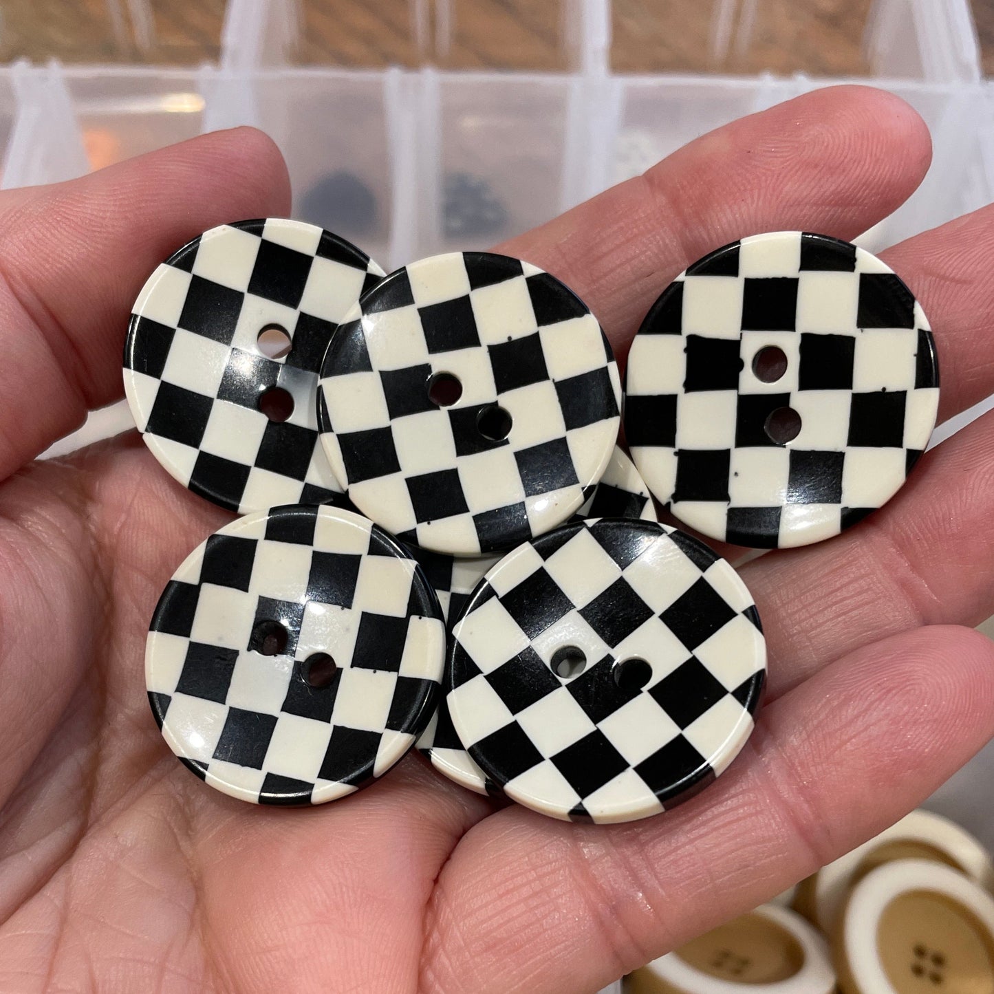 Hand holding three black and white checkered buttons with a container of buttons in the background.