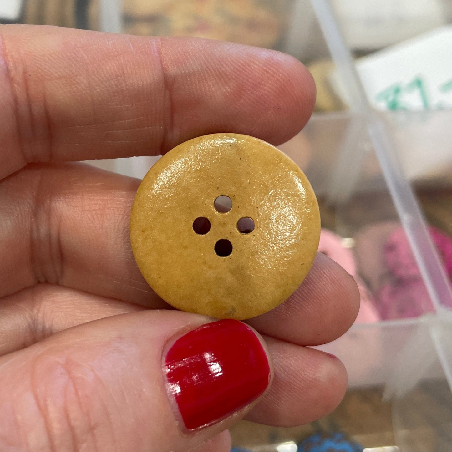 Hand holding a yellow button with a blurred background of a storage box with buttons.