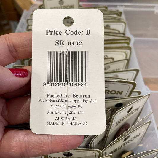 Beutron brand product tag held by a hand with red nail polish, blurred background