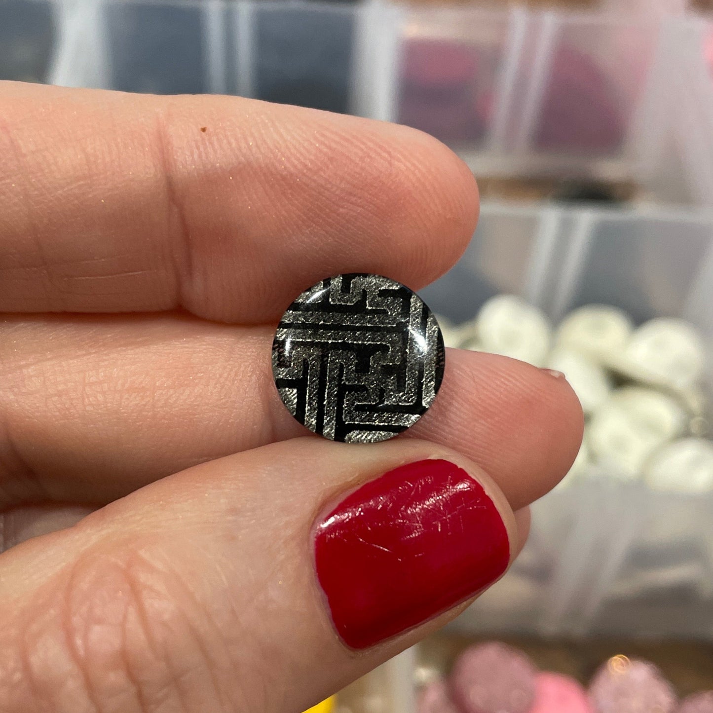 Silver ring with intricate design held by a hand with red nail polish, against a background of craft supplies.
