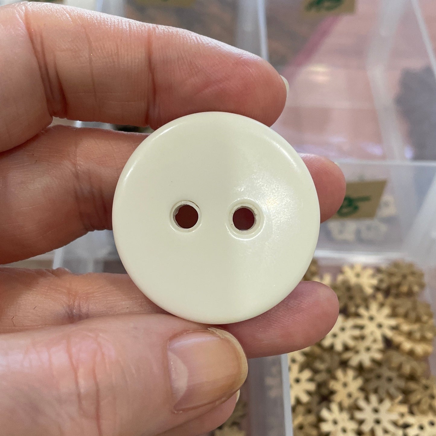 Hand holding a white button with a clear container of small metal gears in the background