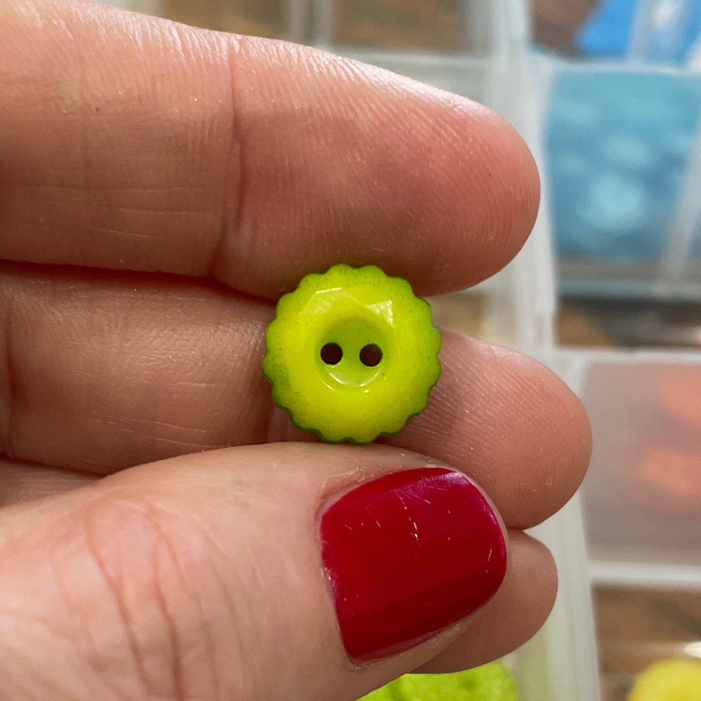 Hand holding two small green buttons with smiley faces against a background of button containers.