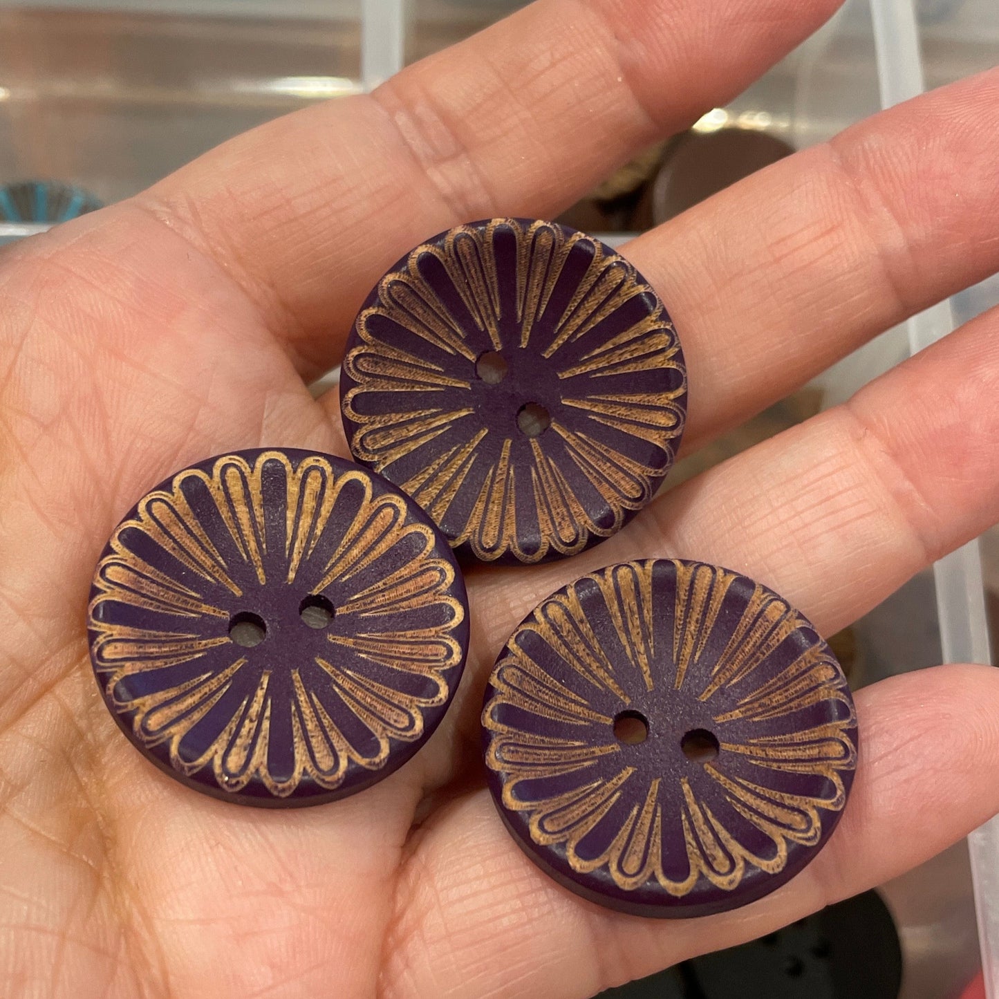 Hand holding three decorative buttons with a clear container of buttons in the background