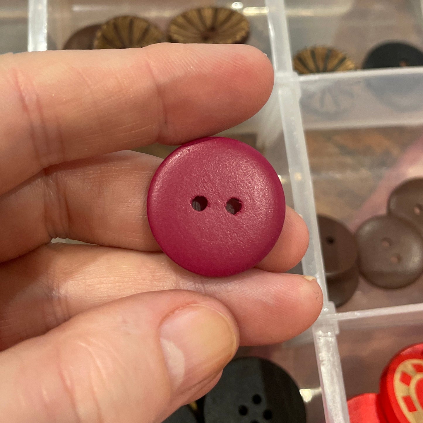Hand holding a purple button with a clear container of buttons in the background