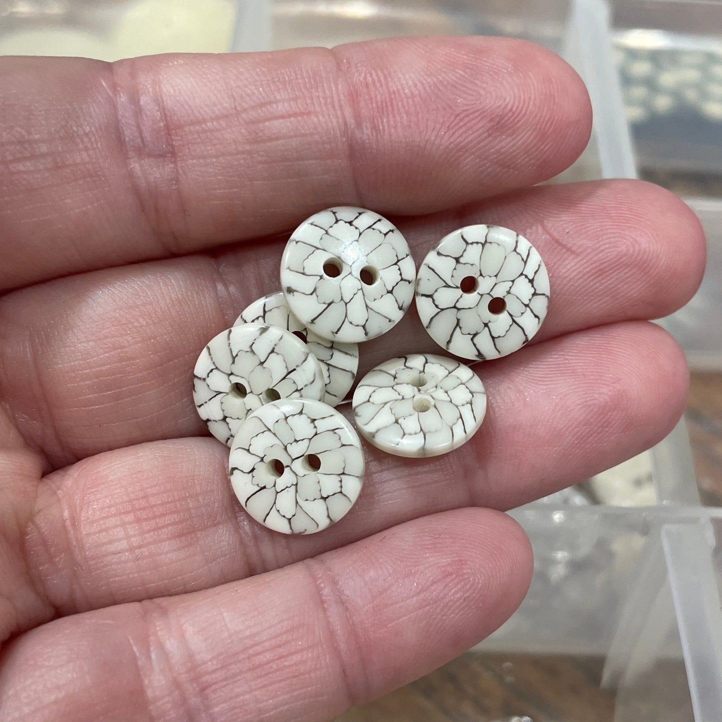Three decorative buttons held in a hand with a clear plastic container in the background.