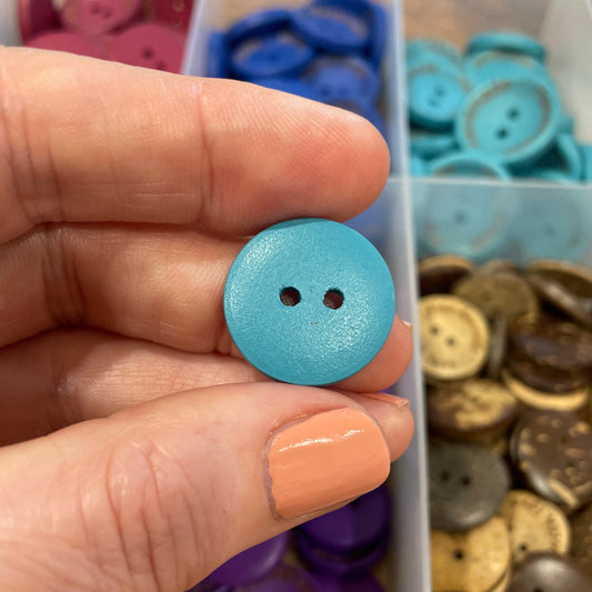 Hand holding a blue button with a container of assorted buttons in the background