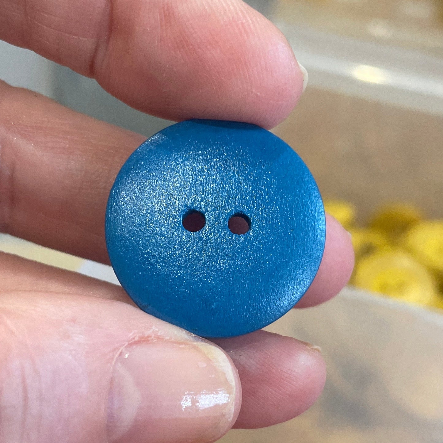 Hand holding a blue button with two holes above a container of orange buttons.