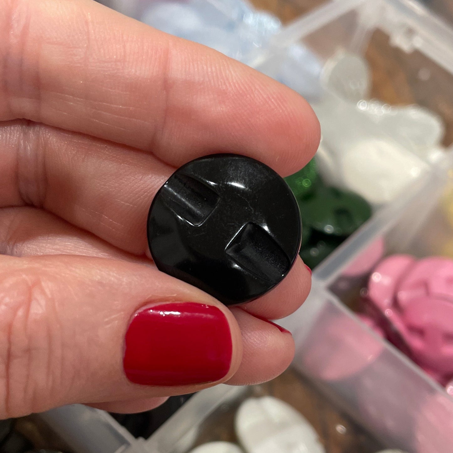 Hand holding a black button with a container of various buttons in the background