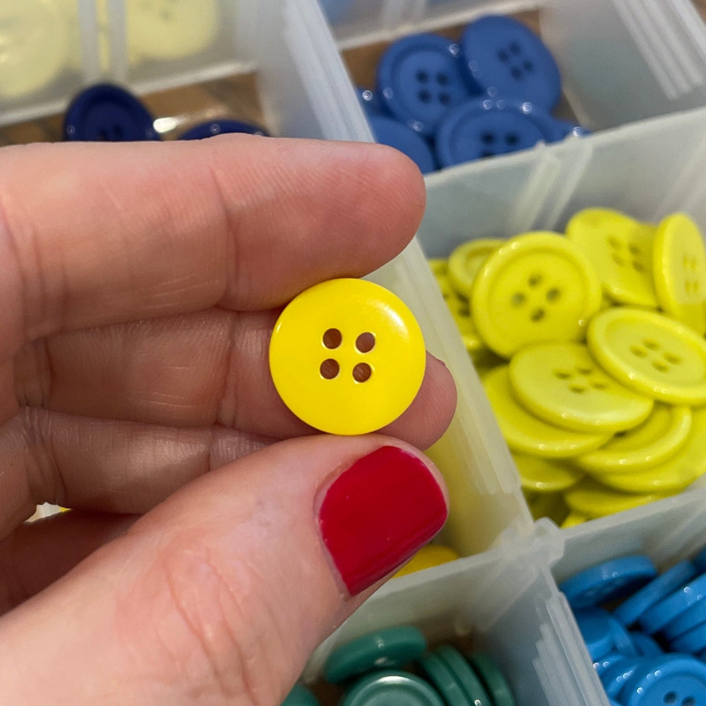 Hand holding a yellow button with a container of colorful buttons in the background