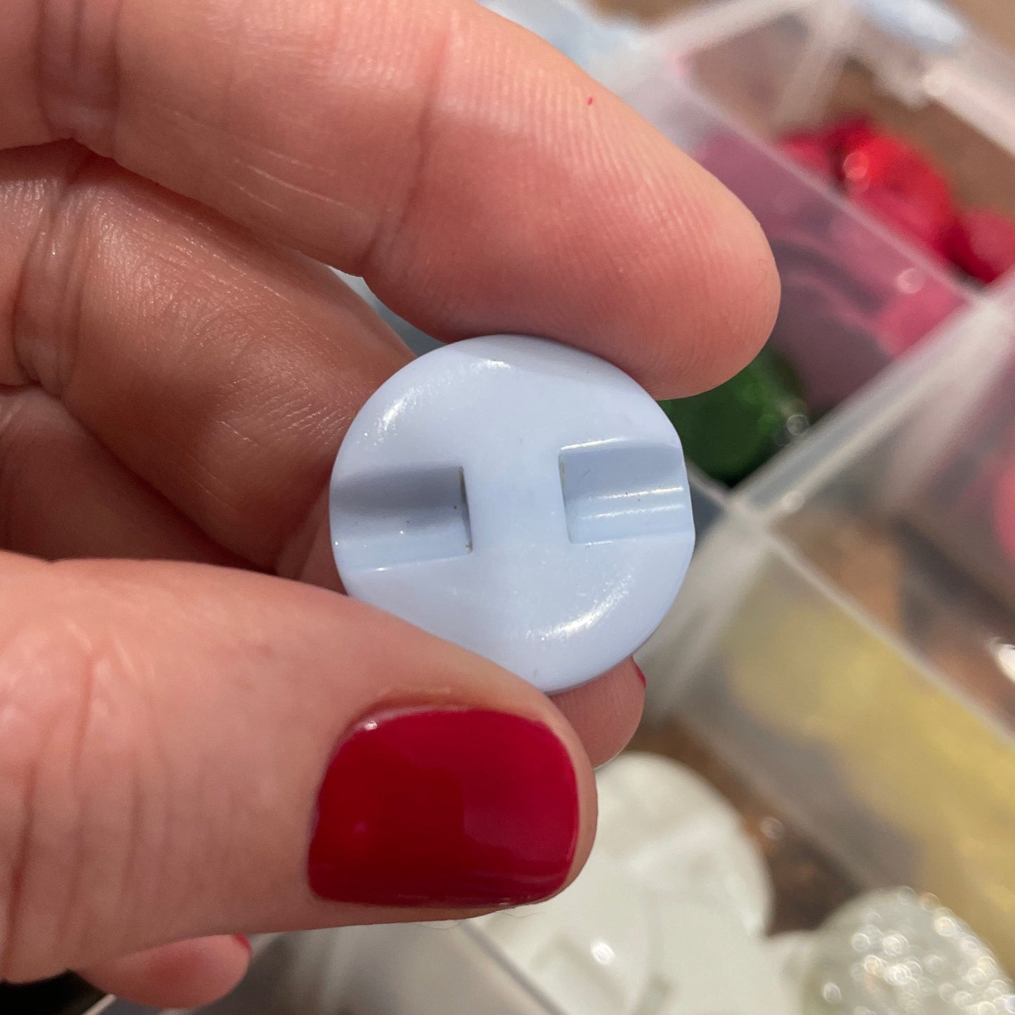 Hand holding a white button with a container of buttons in the background
