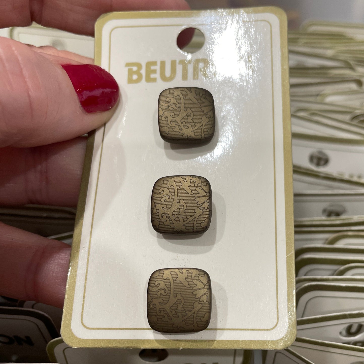 Hand holding a card with three small square buttons labeled 'BEUTON' against a background of similar cards.