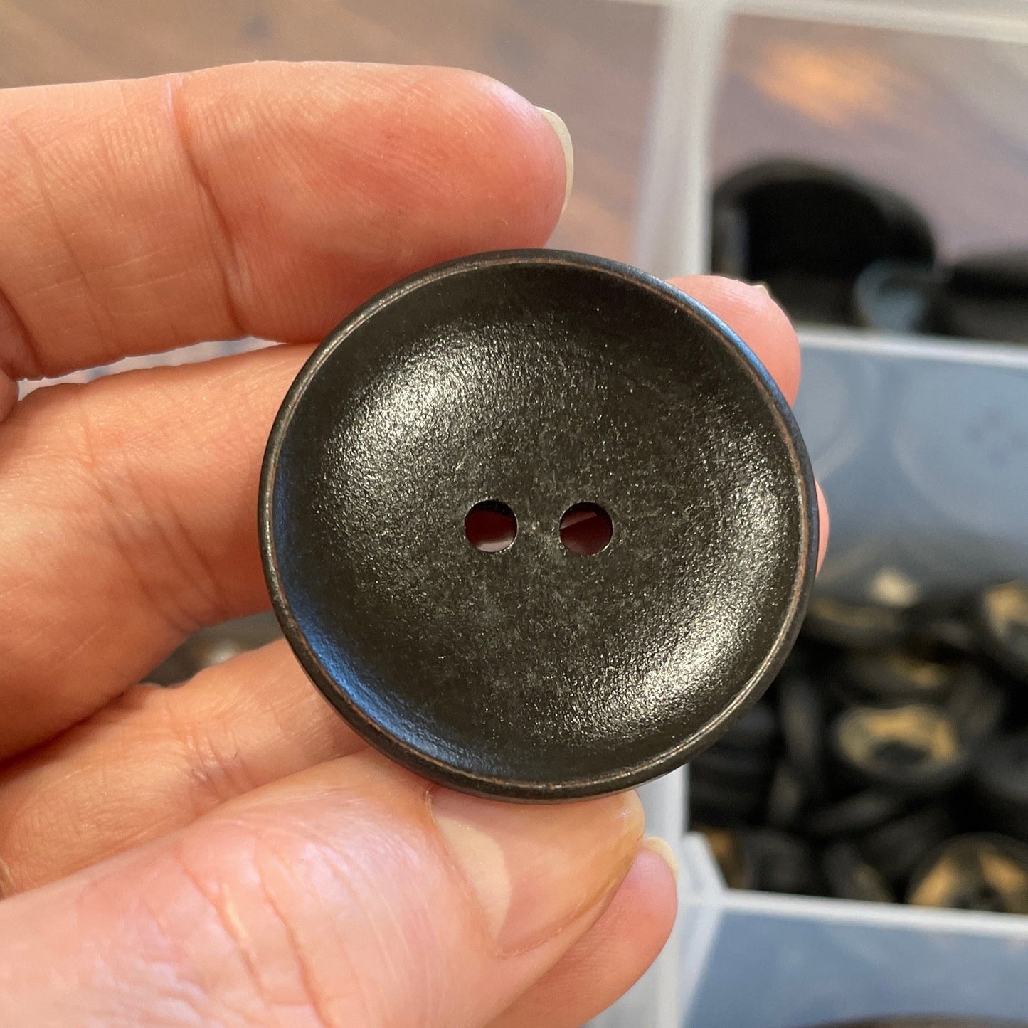 Hand holding a dark brown button with a blurred background of buttons.