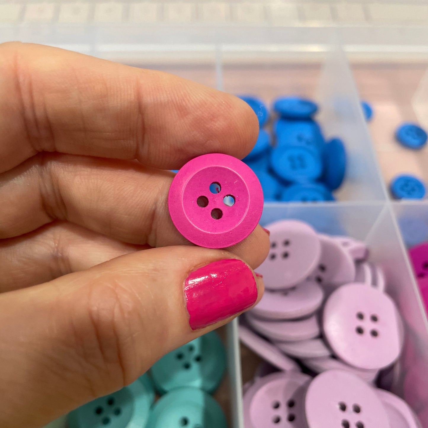 Hand holding a pink button with a container of colorful buttons in the background