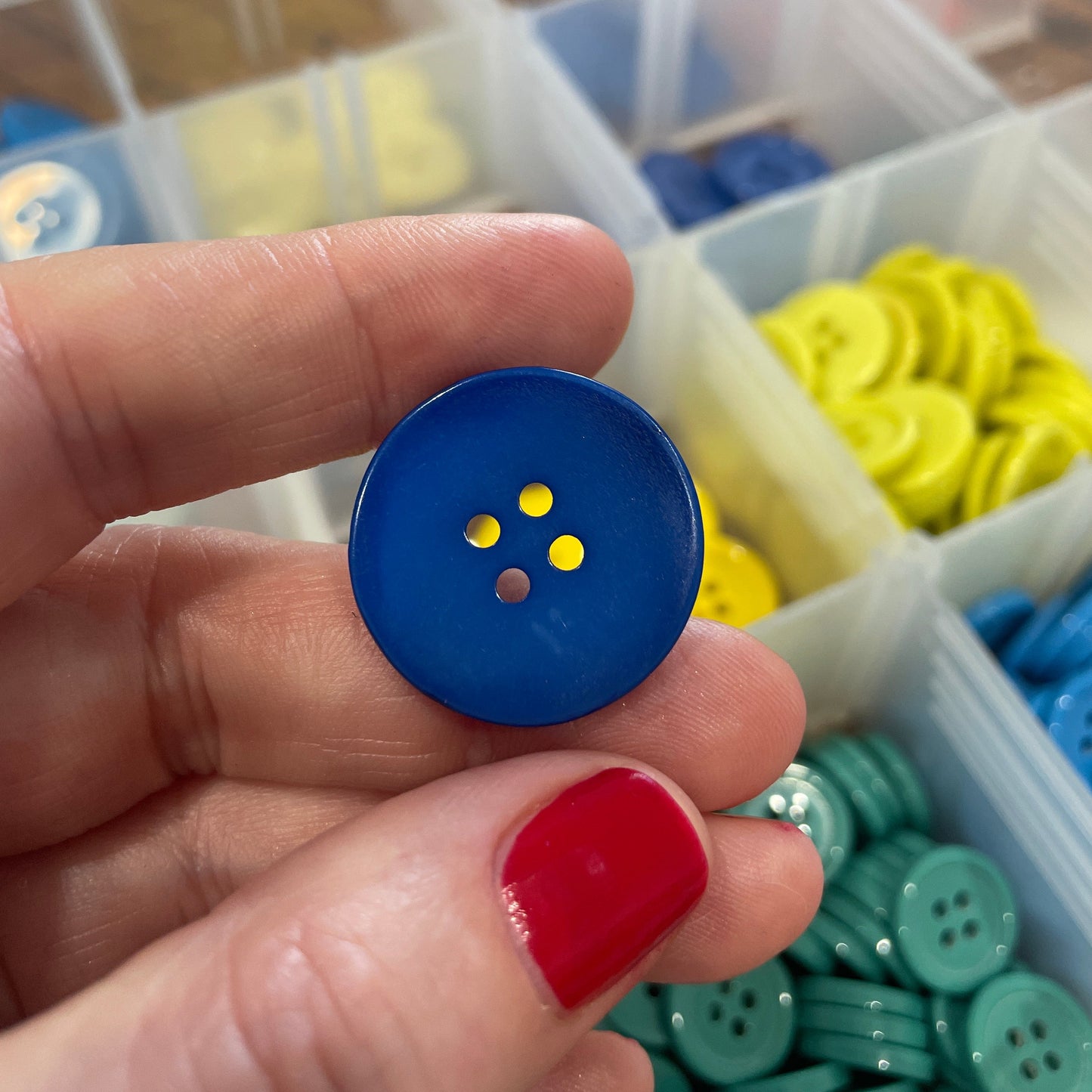 Blue button with yellow centers held between fingers, with button collection in the background