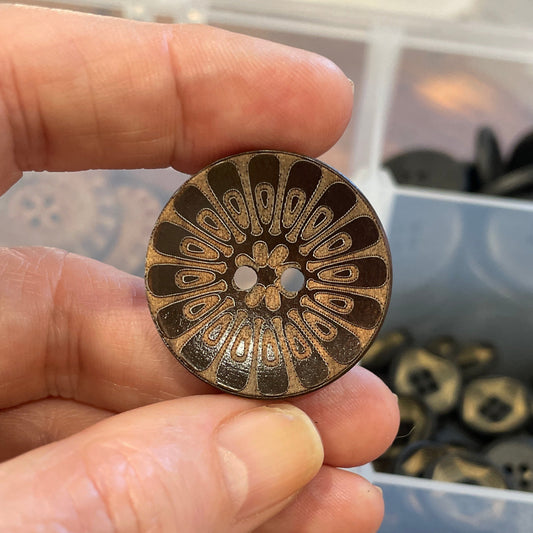 Hand holding a decorative button with intricate design, surrounded by more buttons in the background.