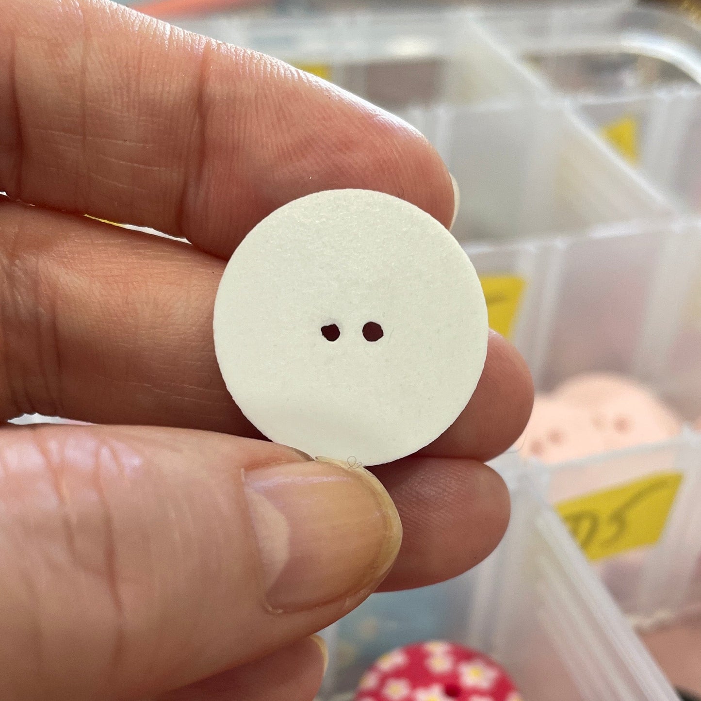 White button held by a hand with a container of buttons in the background