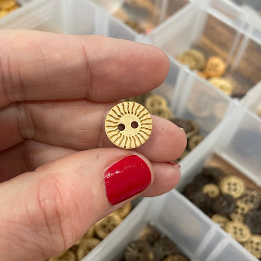 Button held by a hand with red nail polish, against a background of small buttons.