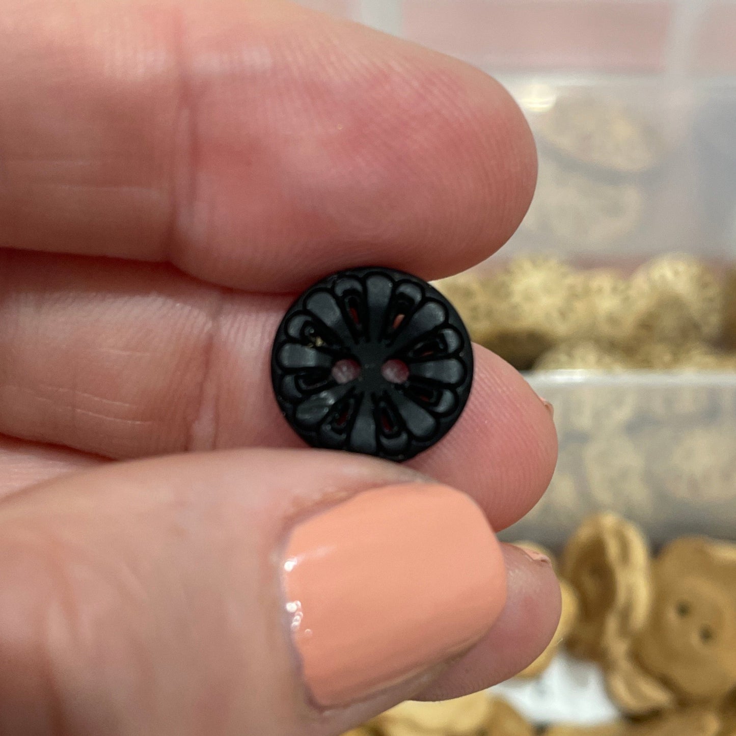 Hand holding a black button with a container of assorted buttons in the background