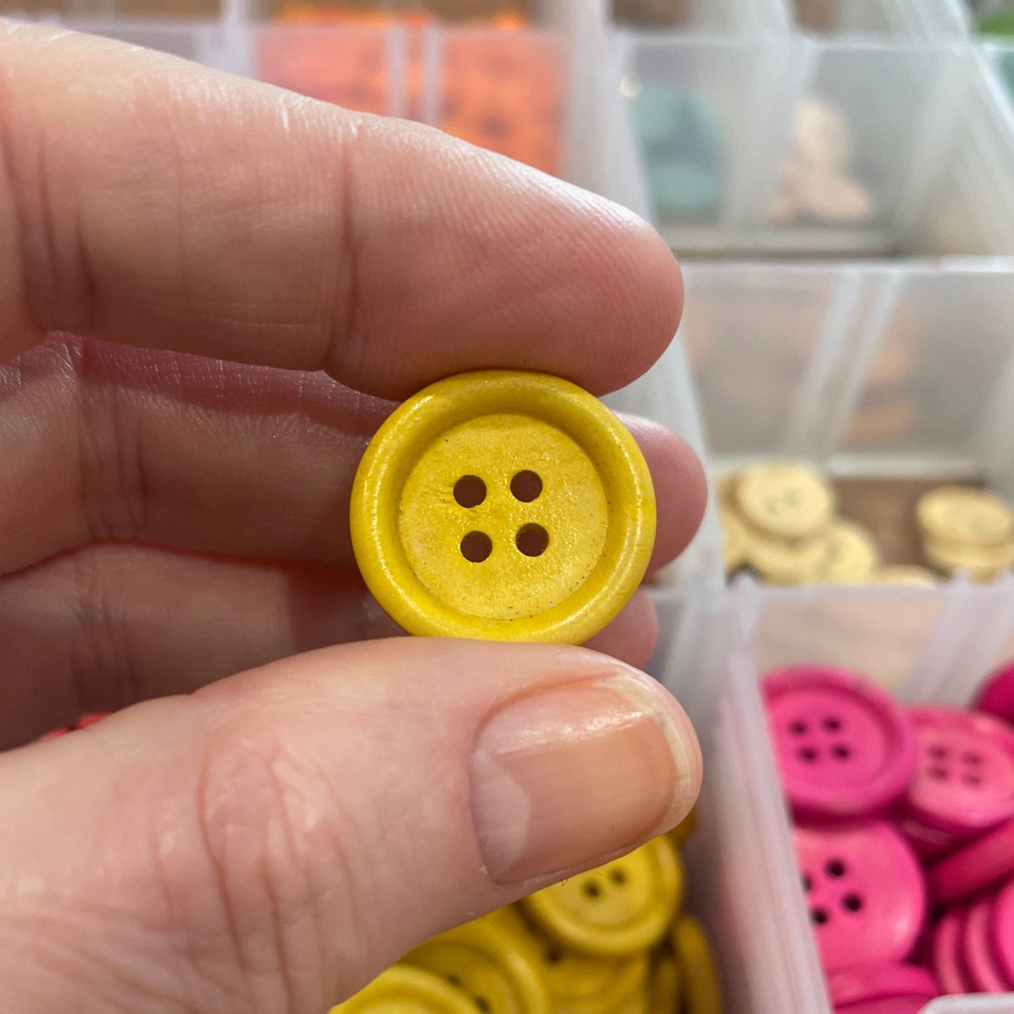 Hand holding a yellow button with a container of buttons in the background