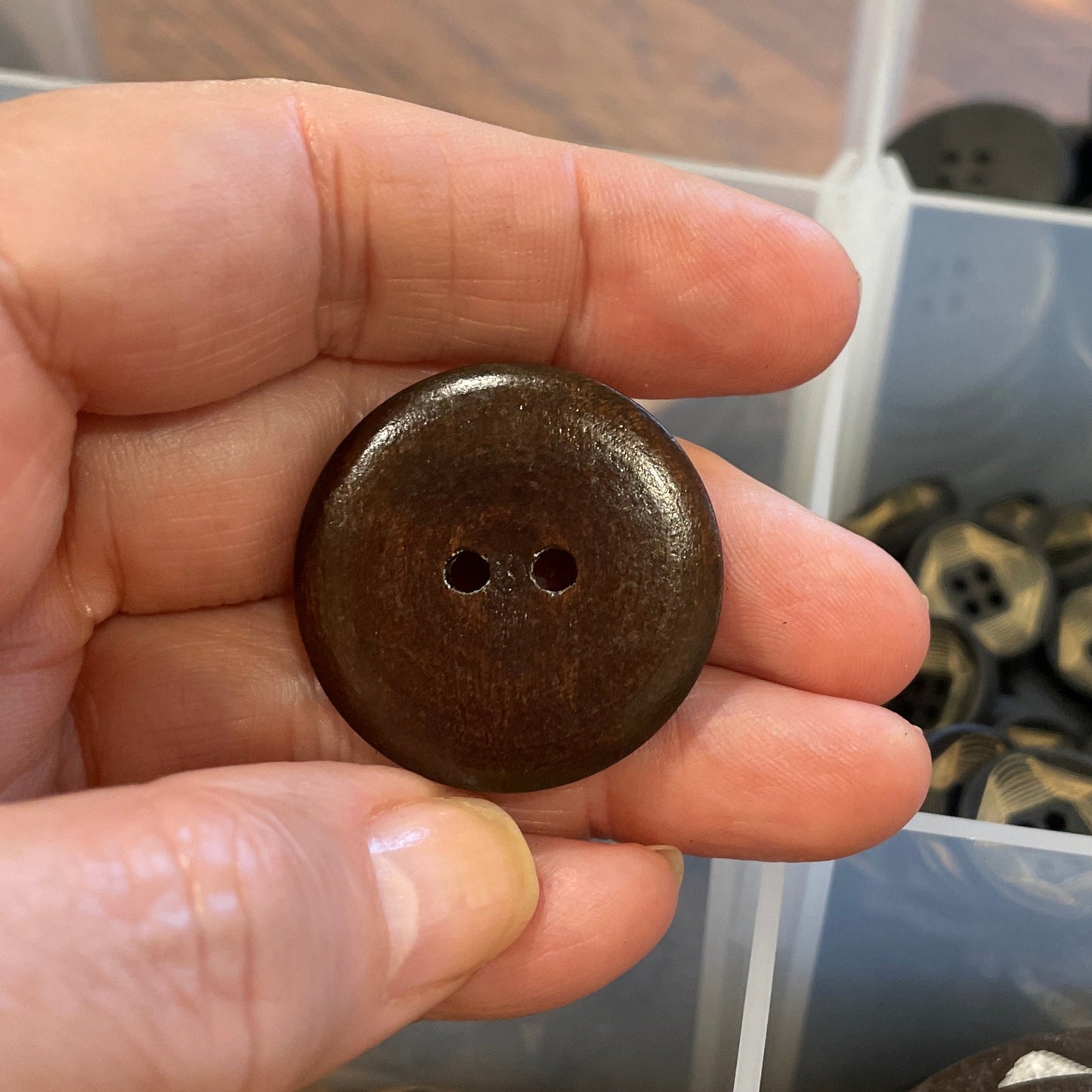 Hand holding a brown button with a container of buttons in the background