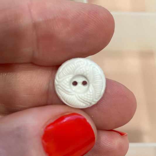 Hand holding a small silver button with a blurred background of buttons