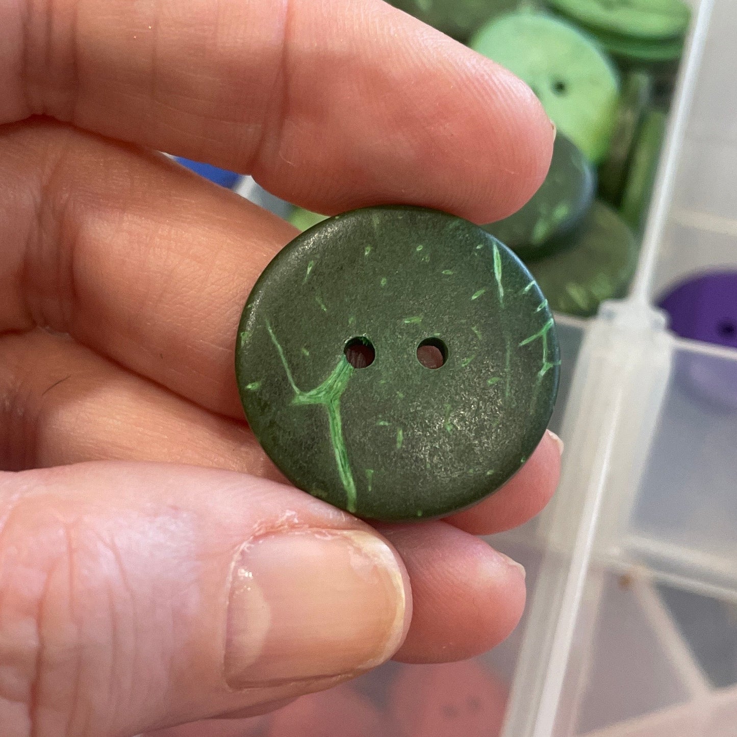 Hand holding a green button with a container of buttons in the background