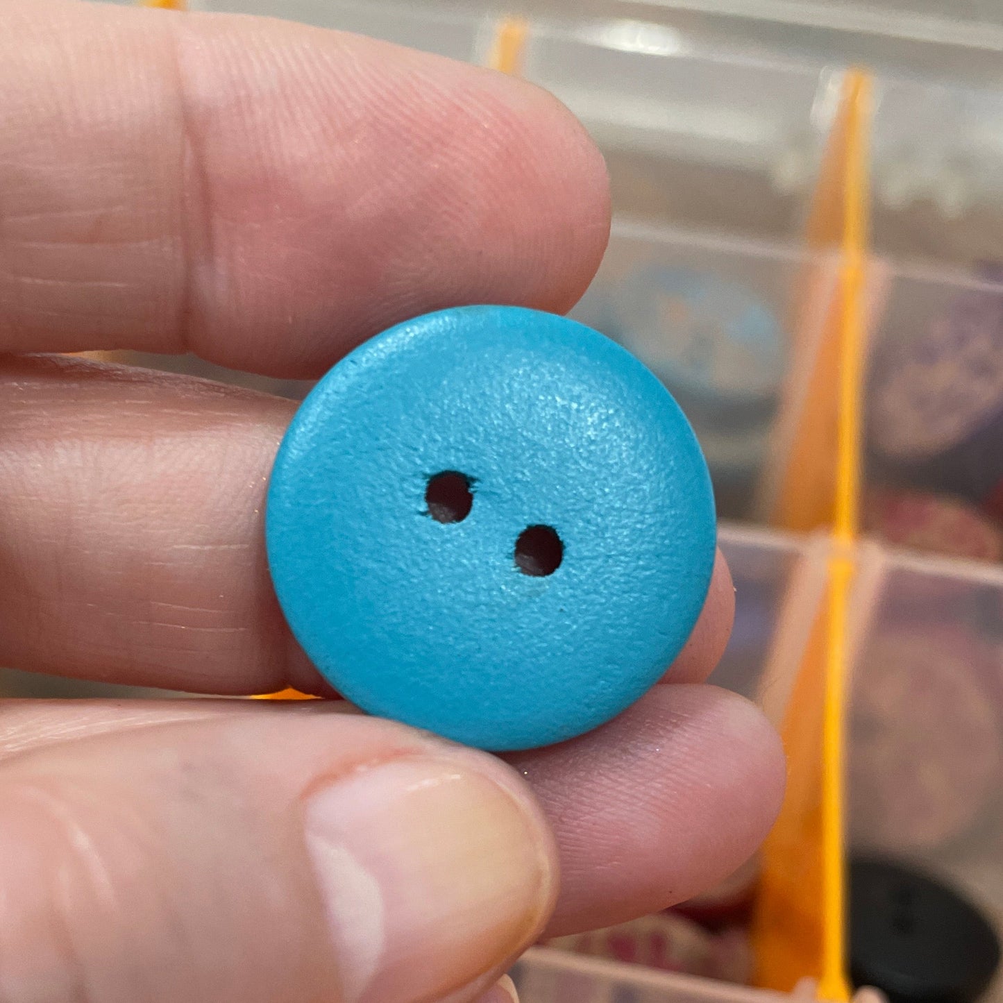 Hand holding a blue button with a clear container of buttons in the background