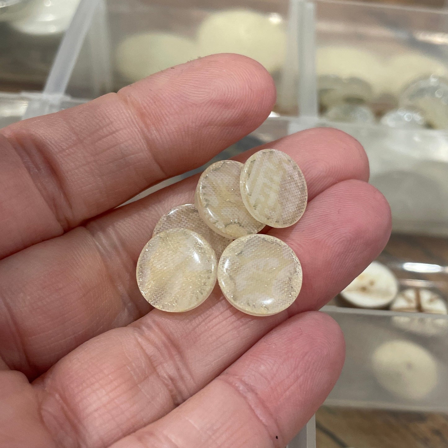 Hand holding four round, clear stones with a blurred background of a jewelry organizer.