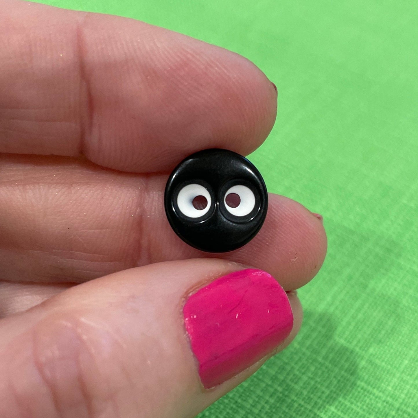 Small black object with white center held between fingers against a green background