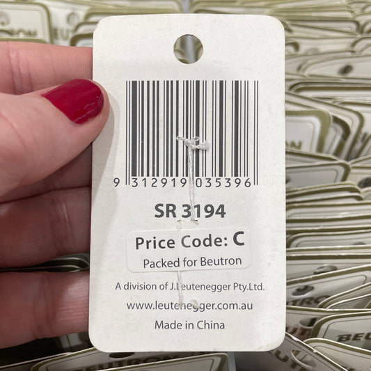 Hand holding a product tag with a barcode and text, with more tags in the background.