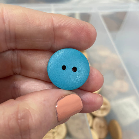 Hand holding a blue button with a clear container of buttons in the background