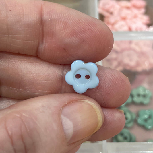Hand holding a small white flower-shaped button with a background of colorful buttons in a box.