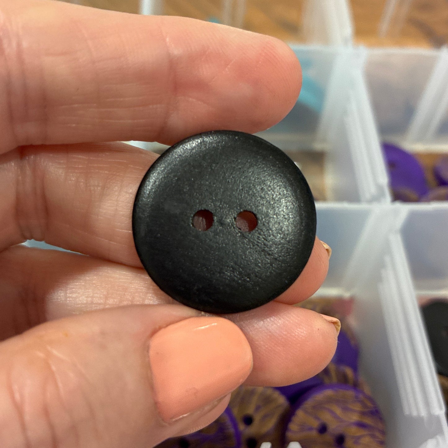 Black button held between fingers with a container of buttons in the background