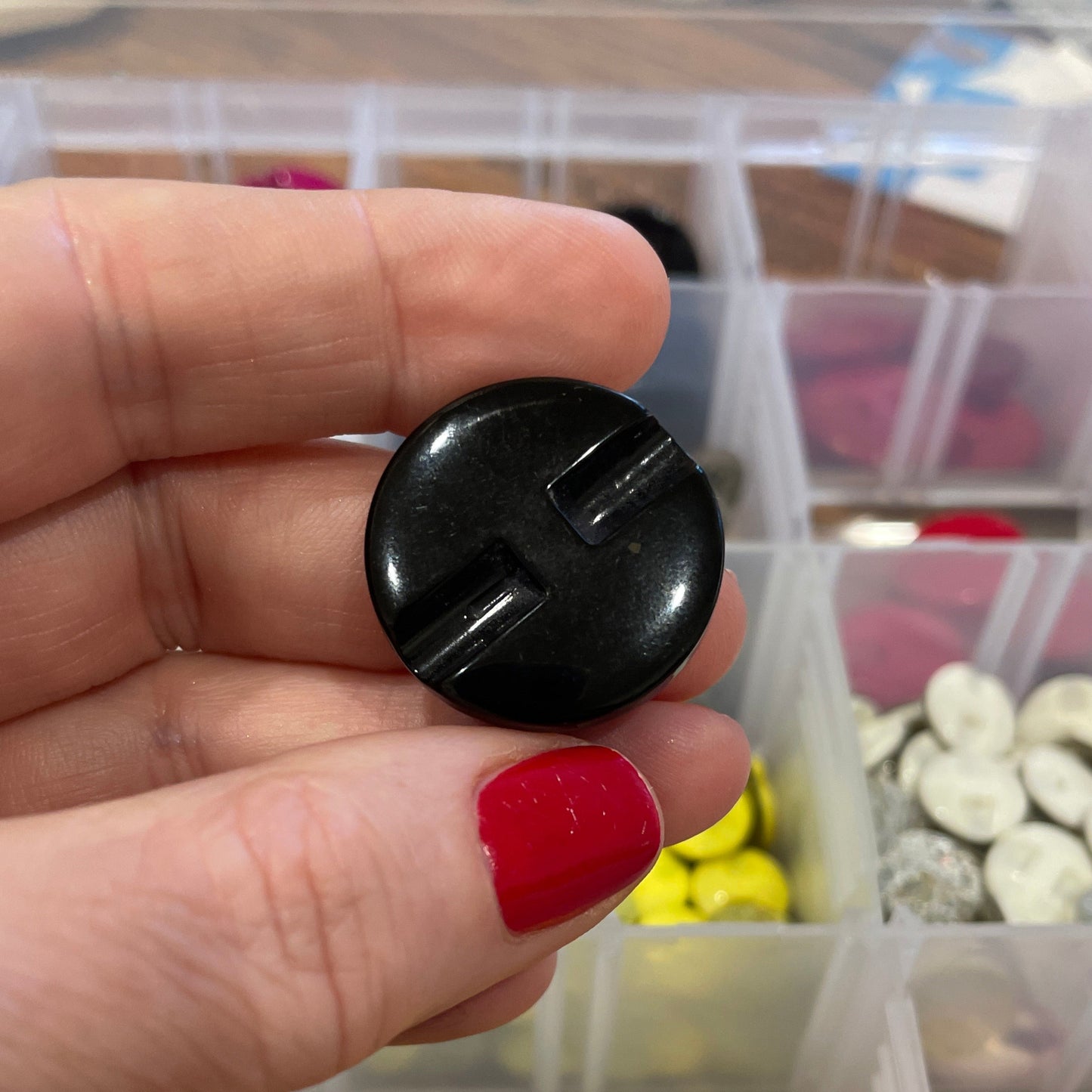 Hand holding a black button with a container of colorful buttons in the background