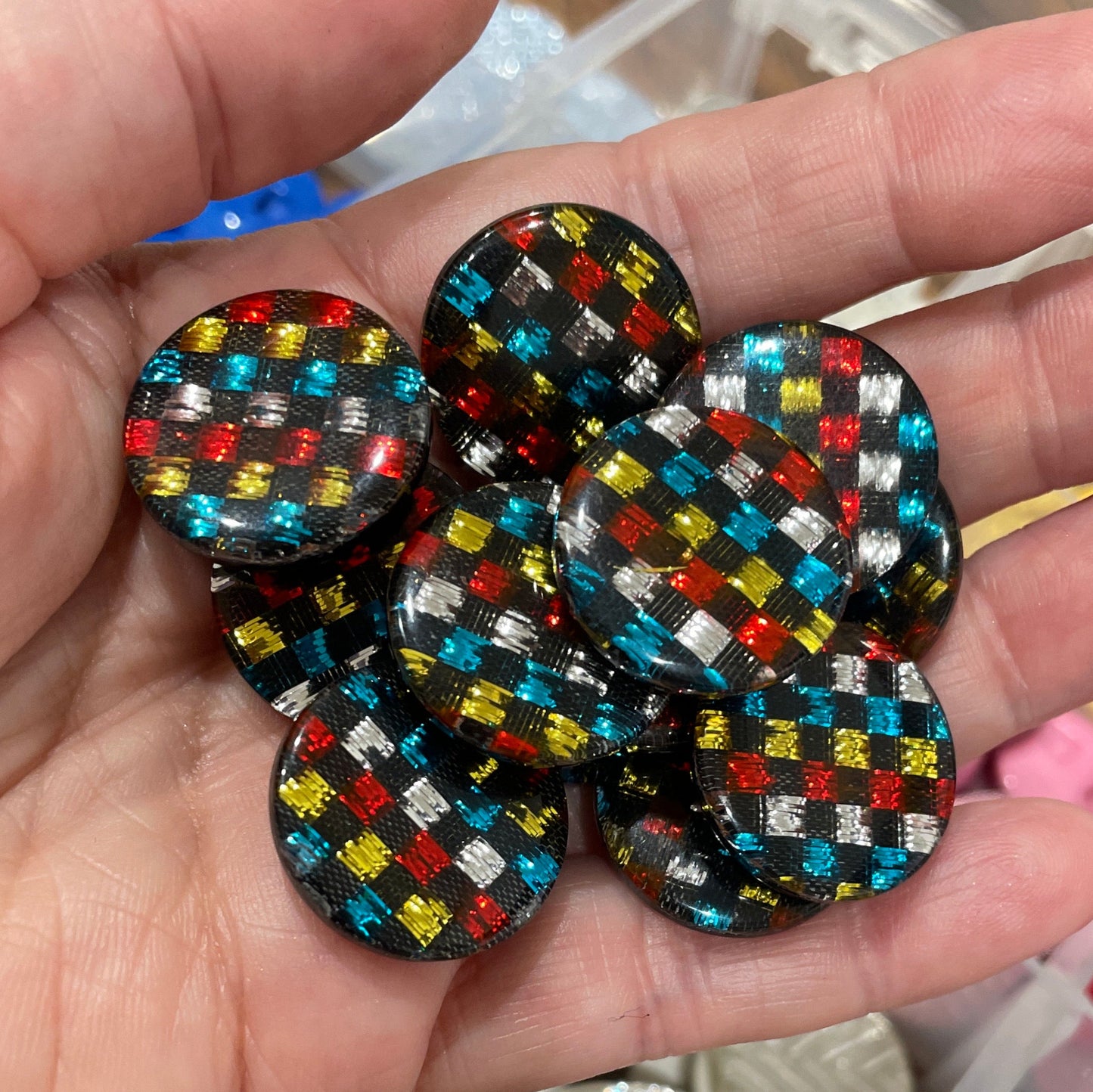 Hand holding colorful buttons with a container of various buttons in the background