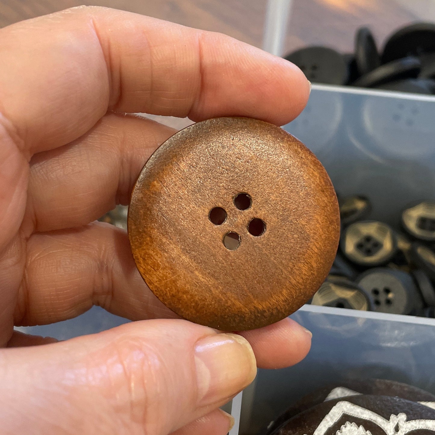 Hand holding a wooden button with a container of buttons in the background