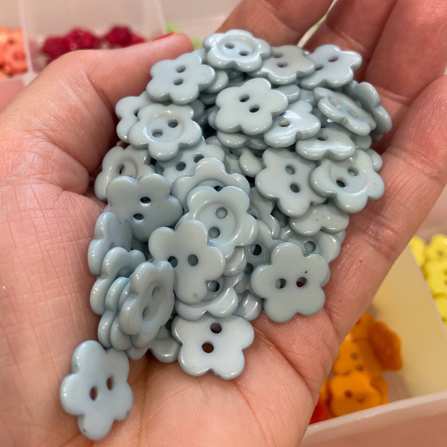 Hand holding a small pile of light blue flower-shaped buttons with a blurred background.