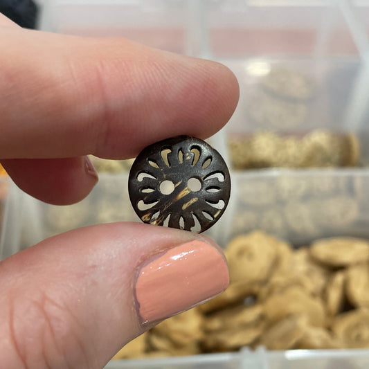 Hand holding a decorative button with a background of various buttons in a container.