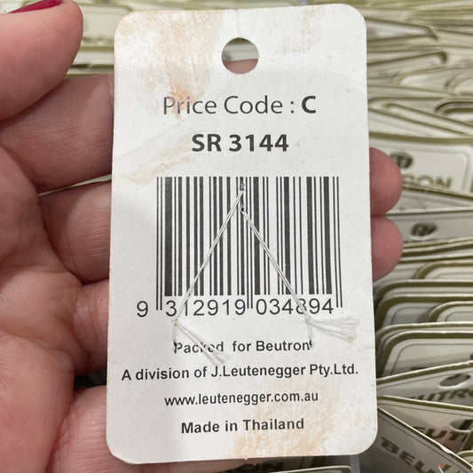 Hand holding a product tag with a barcode and text, with a blurred background of similar tags.